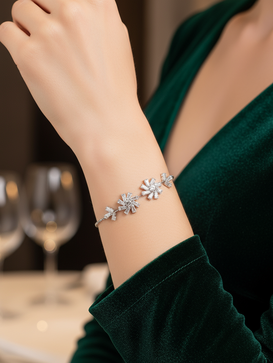 Silver bracelet with floral design on a wrist, wearing a green dress, with blurred background of glasses.