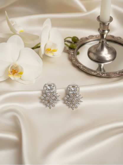 Silver earrings on a white satin surface with a candle and orchids in the background