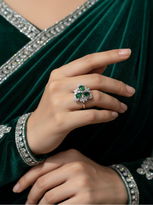 Close-up of a hand wearing an emerald and diamond ring against a green velvet fabric background.